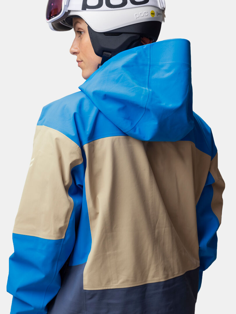 Henkilö, jolla on päällään hiihtokypärä ja sininen ja beige Halti Rizle Unisex 3L DX -laskettelutakki.