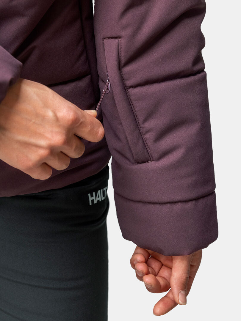 Joku avaa violetin Halti Ascale Puffer Laskettelutakki Naisten hihan taskun, yllään mustat Halti-housut.
