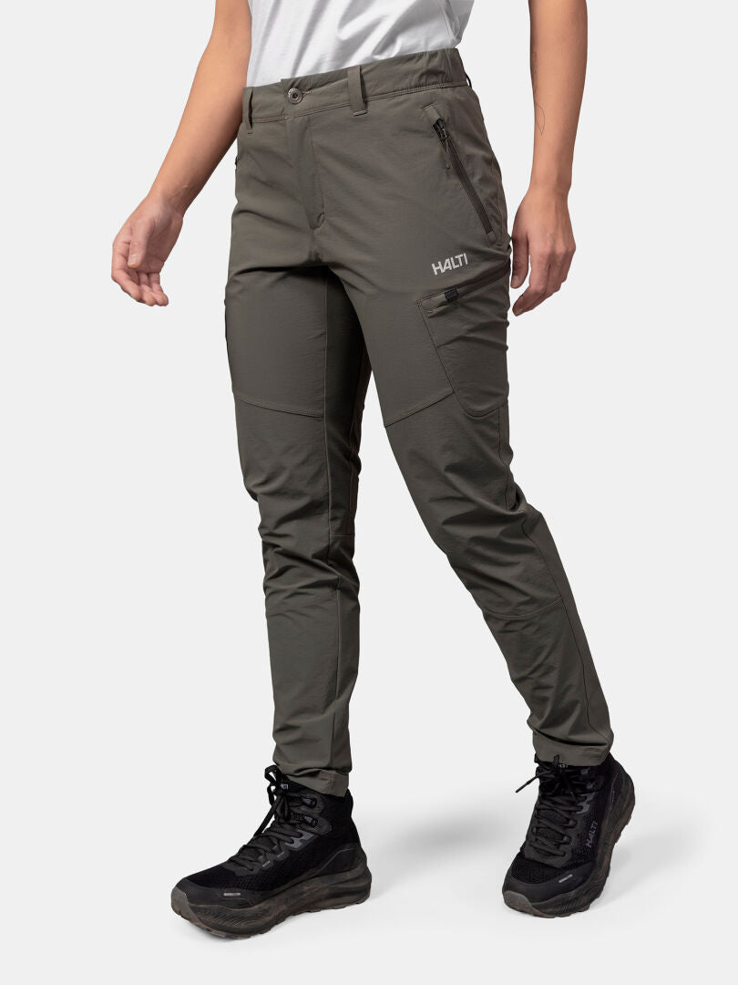 Henkilöllä on oliivinvihreät Halti Pallas Evo X-stretch Housut Naisten ja mustat saappaat yksivärisellä vaaleanharmaalla pohjalla.
