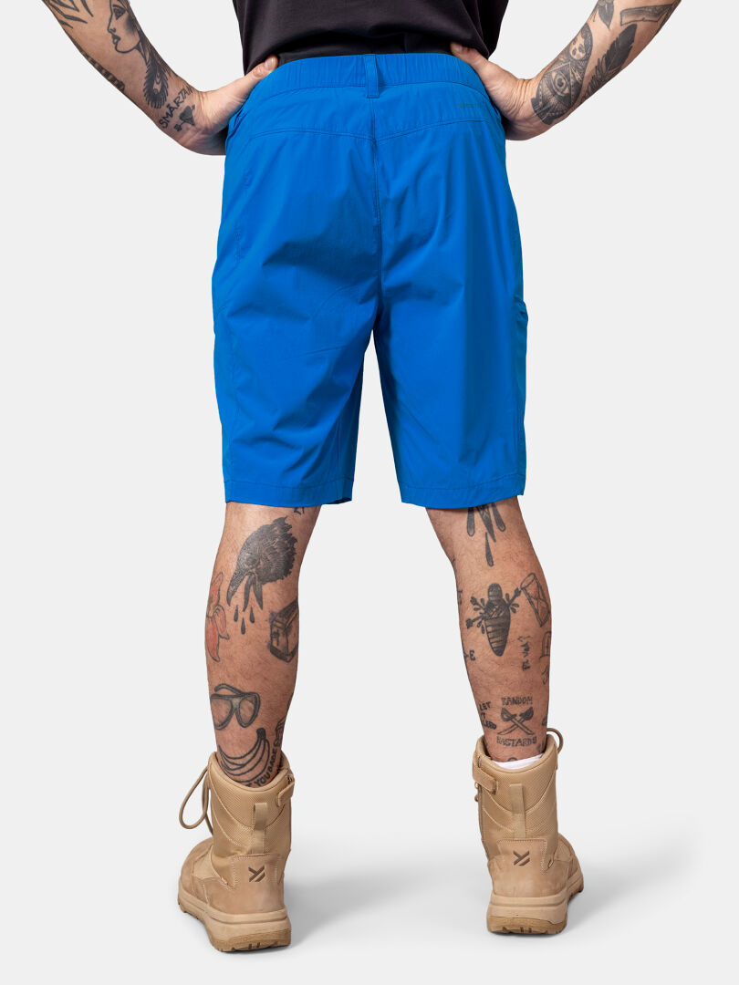 Henkilö, jolla on Halti Pallas Cool X-stretch Shortsit Miesten ja ruskehtavat saappaat, seisoo selkä kameraan päin ja näyttää jalkatatuoinnit.