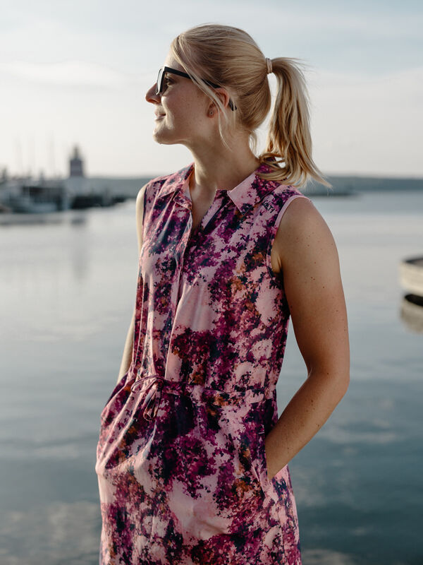 Halti Chipper X-stretch Mekko Naisten aurinkolaseissa ja aurinkolaseissa oleva nainen seisoo veden rannalla kädet taskuissa.