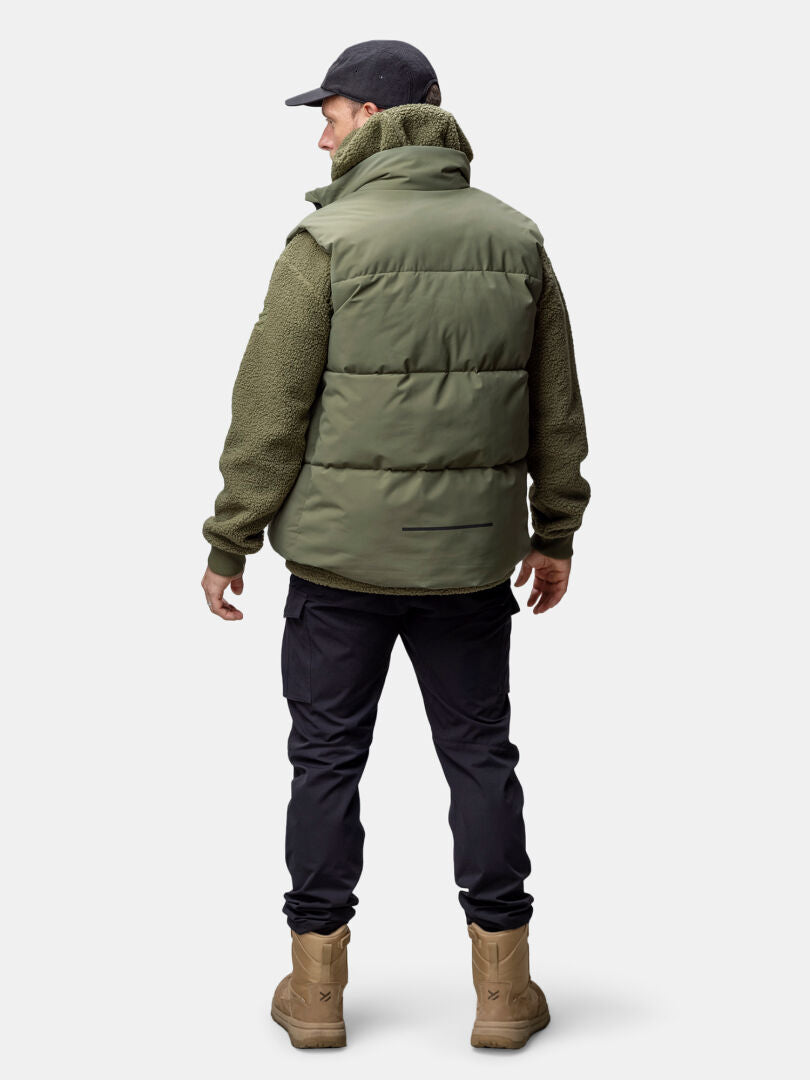 Henkilö, jolla on vihreä Halti Penger Classic Puffer Liivi Miesten, oliivinvärinen takki, mustat housut, ruskehtavat saappaat ja musta lippis, selkä näkyvissä.