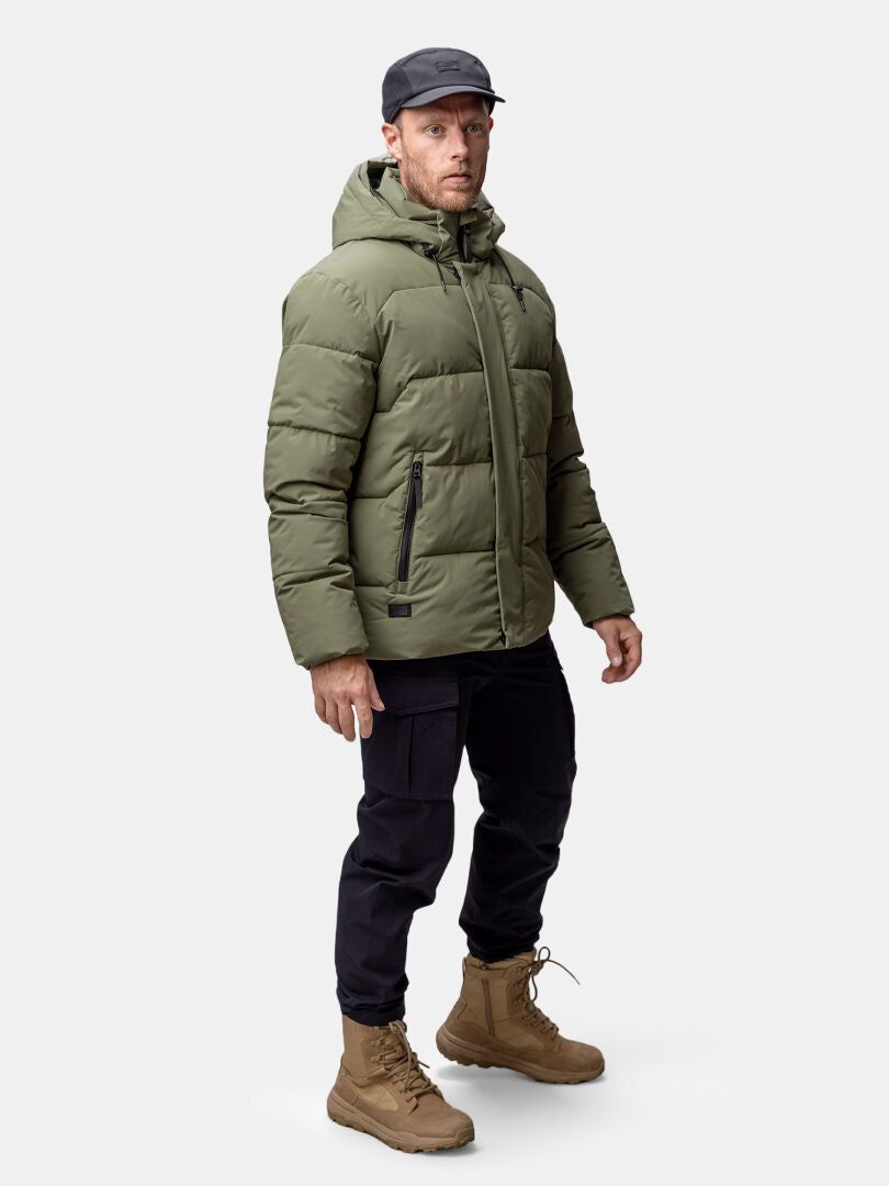 Miehellä on yllään Halti Brahe Puffer Talvitakki Miesten oliivinvihreä, mustat housut ja ruskehtavat saappaat.