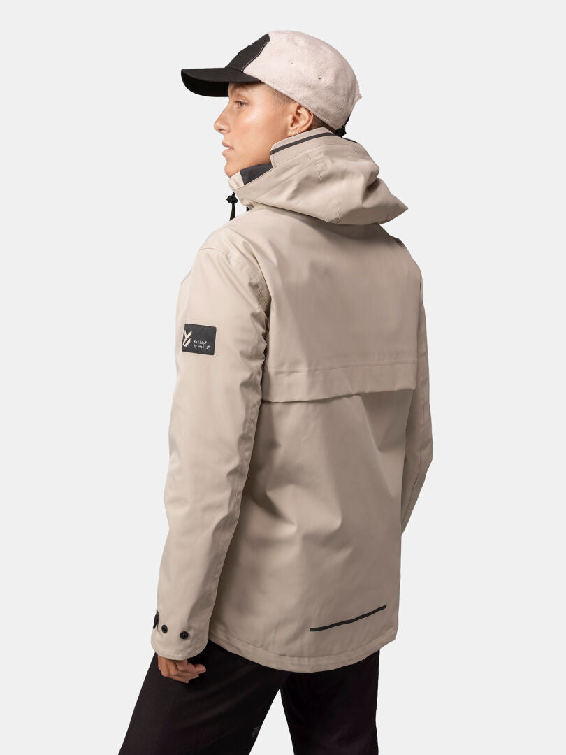 Henkilöllä on yllään beige Halti Tokoi DX Takki Naisten ja lippis, hän seisoo selkä kameraan päin.