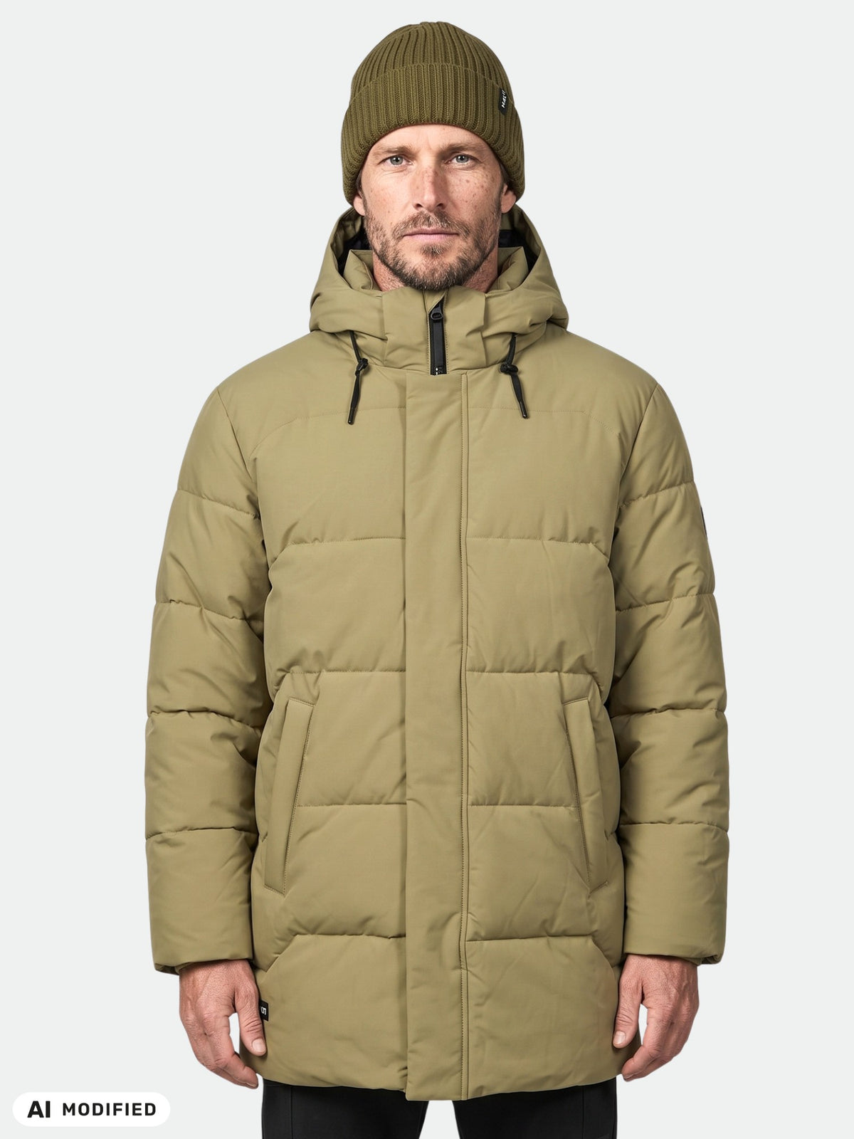 Mies, jolla on yllään Halti Brahe Puffer Parka Miesten -takki ja pipo, seisoo kasvot kameraan päin vaalealla yksivärisellä taustalla.