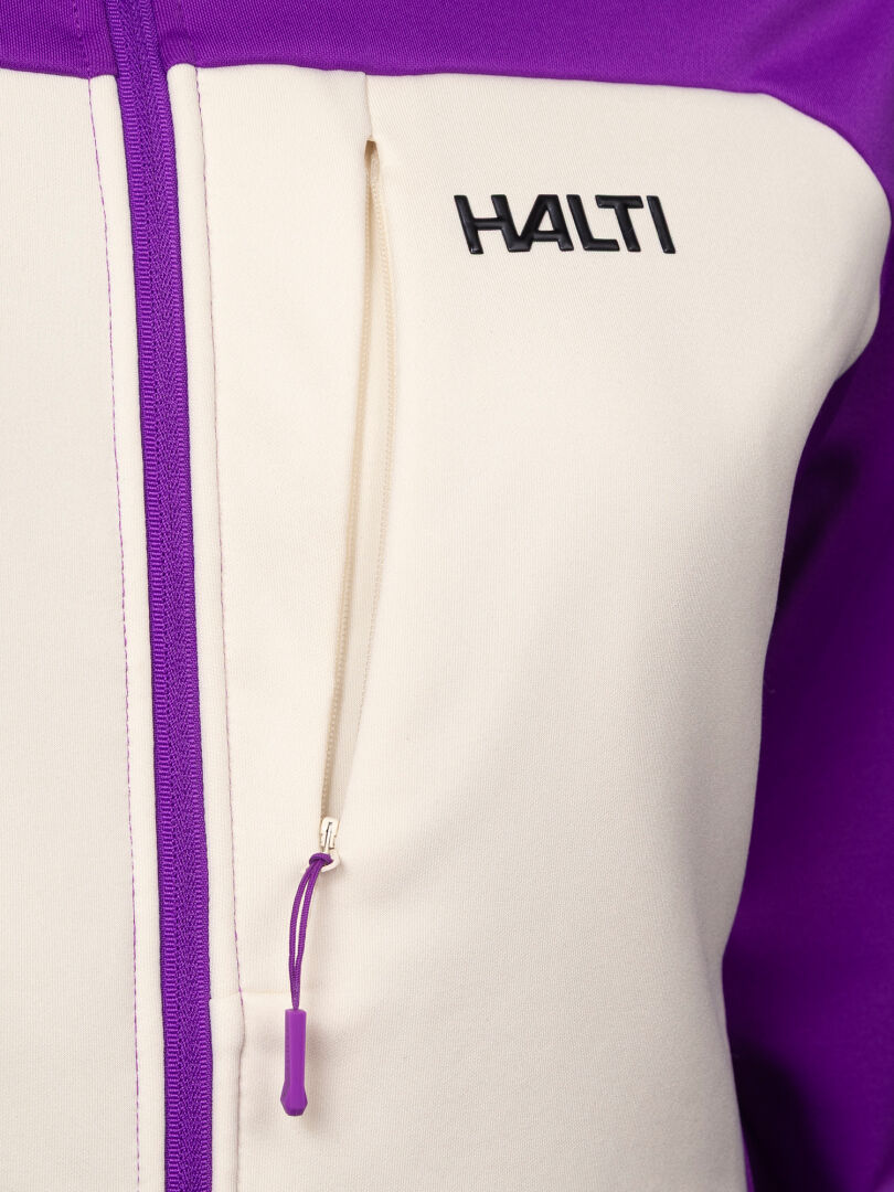 Lähikuva valkoisesta ja violetista Halti Seiland Välitakki Naisten -fleece-takista, jossa on vetoketjullinen rintatasku ja logo.