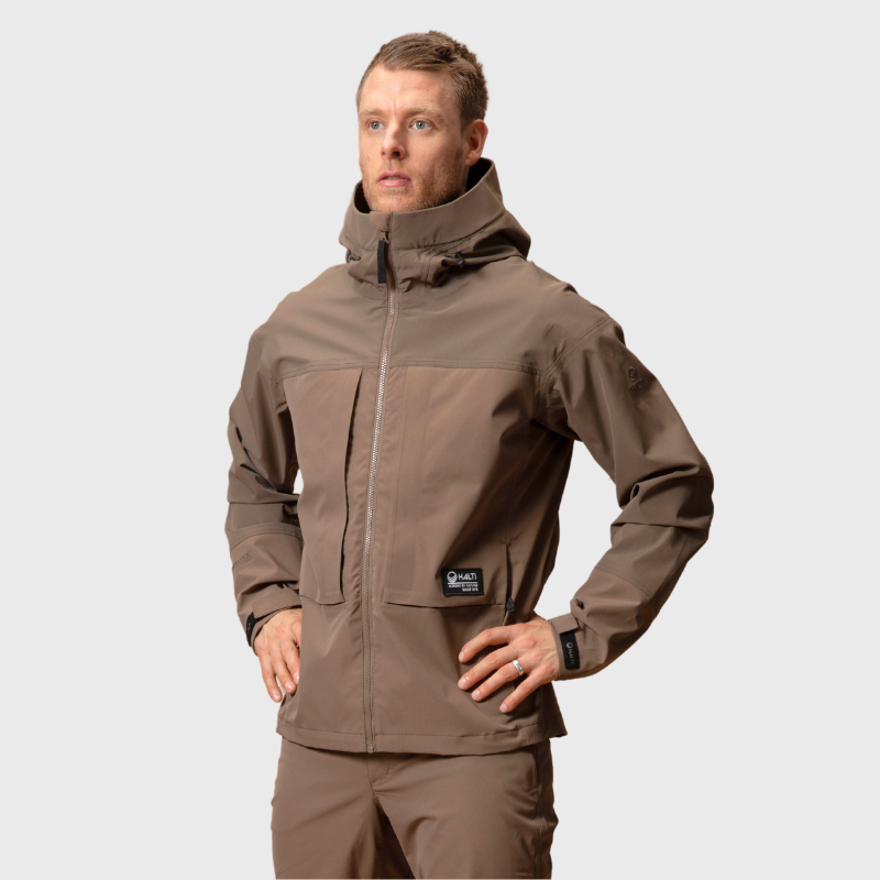 Ruskeassa Halti Hiker II DrymaxX Kuoritakki -takissa ja yhteensopivissa housuissa oleva mies seisoo toinen käsi lantiolla.