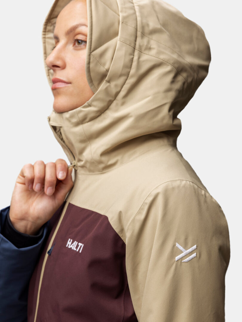 Henkilö, jolla on beige Halti Gracer DX laskettelutakki, ruskeankeltainen rinta, valkoinen hihalogo, sivulta katsottuna.