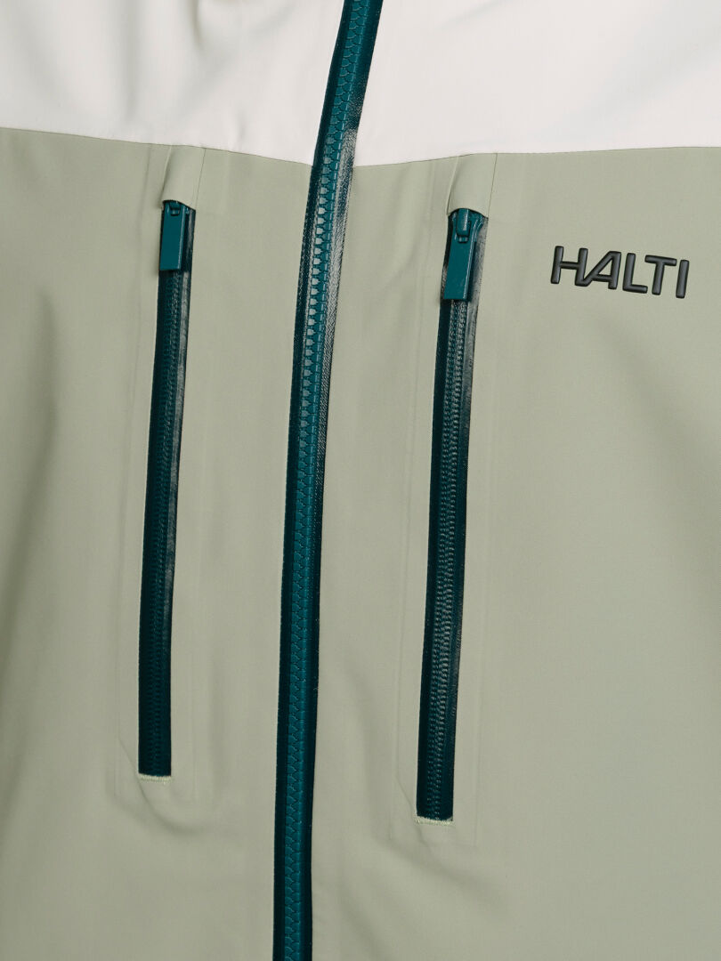 Lähikuva kaksivärisestä Halti Rizle Unisex 3L DX -laskettelutakista, jossa on keskellä vetoketju, kaksi pystysuoraa rintataskua ja logo.