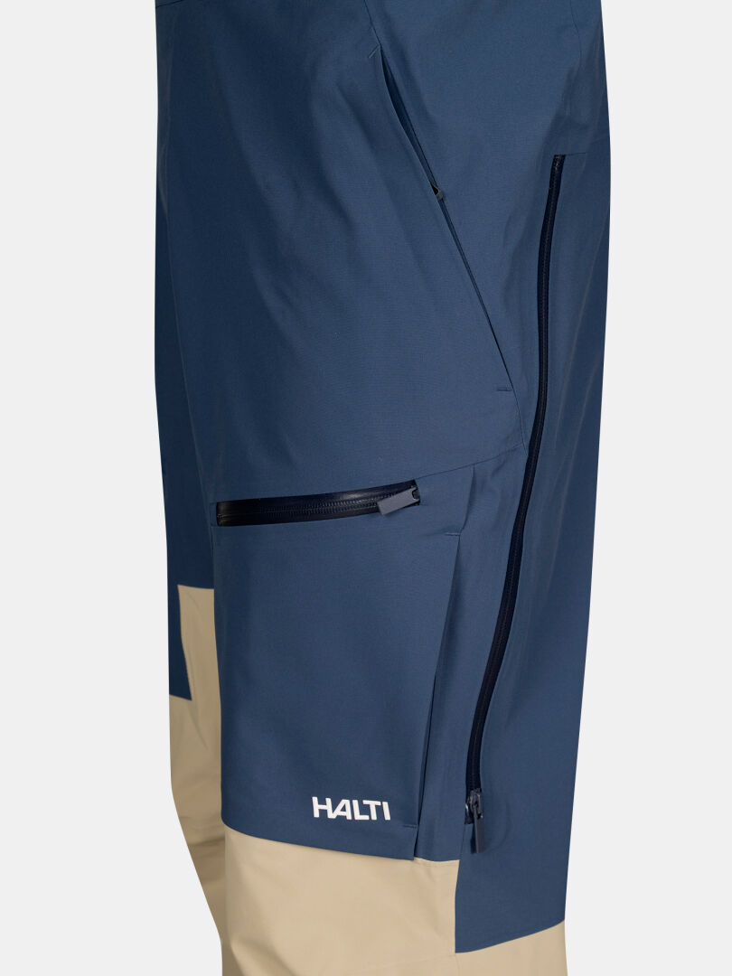 Lähikuva Halti Rizle 3L DX unisex-hiihtohousuista, väri sininen/beige, vetoketjulliset taskut ja logo polven lähellä.