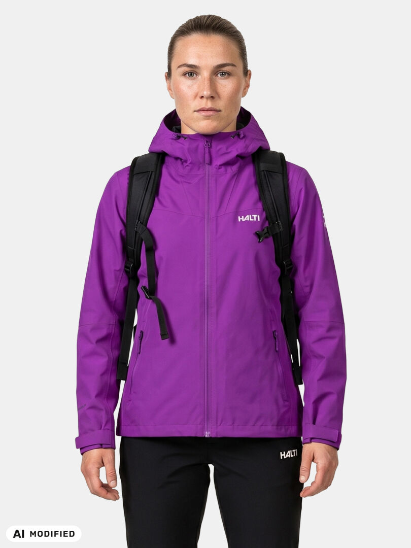 Nainen, jolla on yllään violetti Halti Forter DX Kuoritakki -takki ja mustat housut sekä musta reppu, valkoisella taustalla.
