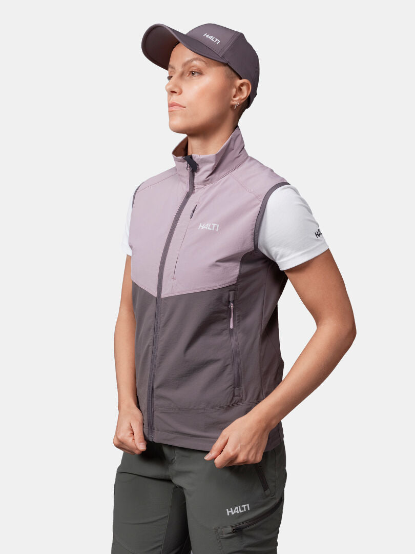 Henkilö, jolla on violetti lippis, Halti Pallas Evo X-stretch Liivi Naisten, valkoinen t-paita ja harmaat housut, seisoo vasemmalle päin.