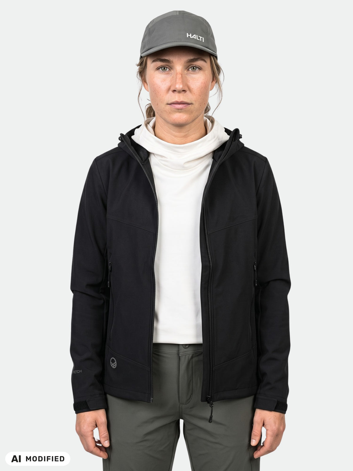 Henkilö, jolla on yllään musta Halti Pallas Evo Brushed X-stretch Takki Naisten -takki, valkoinen turtleneck-paita, oliivinvihreät housut ja harmaa lippalakki.