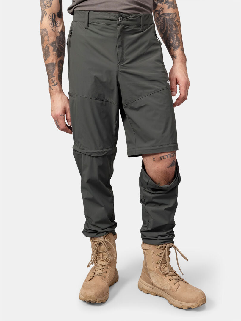 Henkilöllä on ruskehtavat taistelusaappaat ja Halti Pallas Cool Stretch Zip-off Housut Miesten, jonka toinen jalka on osittain vetoketjulla suljettu.