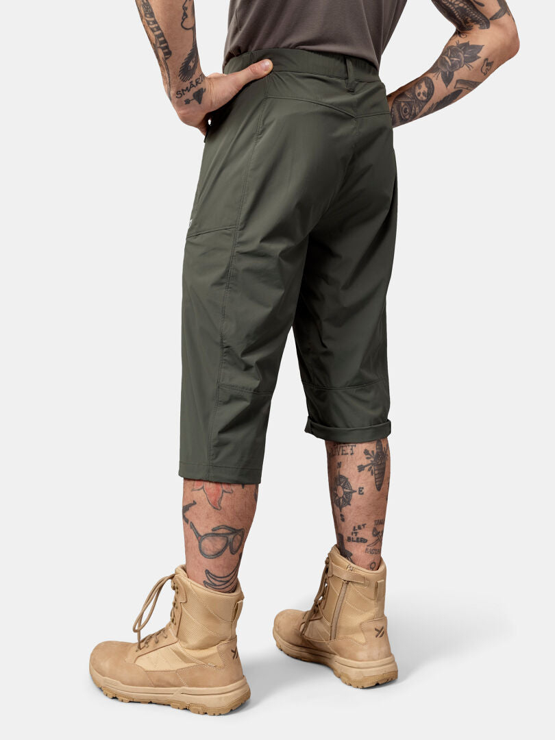 Henkilöllä Halti Pallas Cool X-stretch Caprit, ruskehtavat saappaat, harmaa paita, käsivarsien ja jalkojen tatuoinnit näkyvissä.