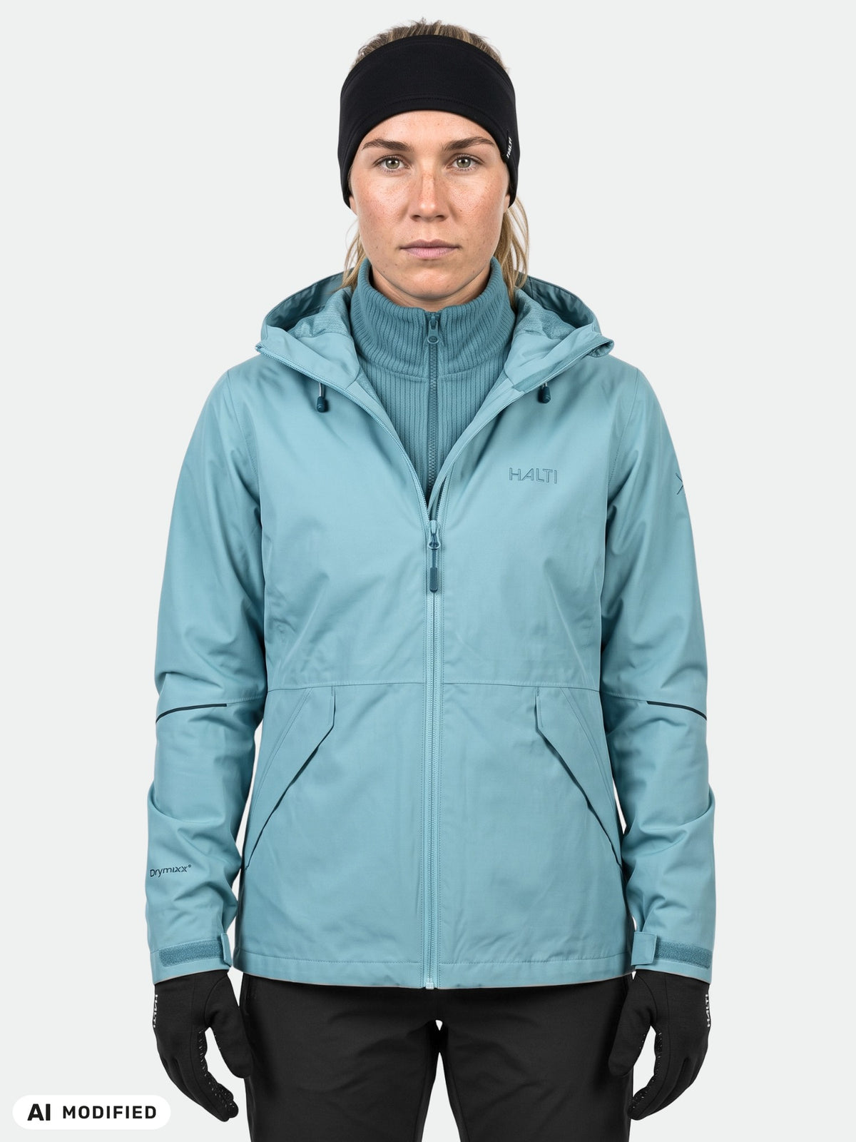 Henkilö, jolla on yllään sininen Halti Loito 3in1 DX -takki, mustat käsineet, pääpanta ja sininen turtleneck-paita, katsoo eteenpäin.