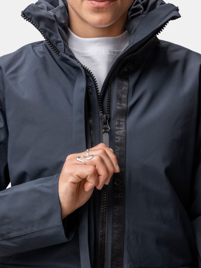 Henkilö vetää vetoketjun Halti Synkas 3in1 DrymaxX Parka Naisten valkoisen poolokauluksen päälle ja näyttää hopeasormuksen.