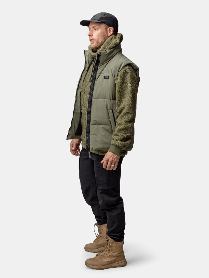 Profiilissa olevalla miehellä on Halti Penger Classic Puffer -liivi, fleecetakki, mustat housut, ruskehtavat saappaat ja musta lippis.