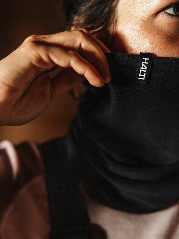 Henkilö, joka vetää mustan Halti Trone Fleece Tuubihuivi -huivin nenänsä yli.