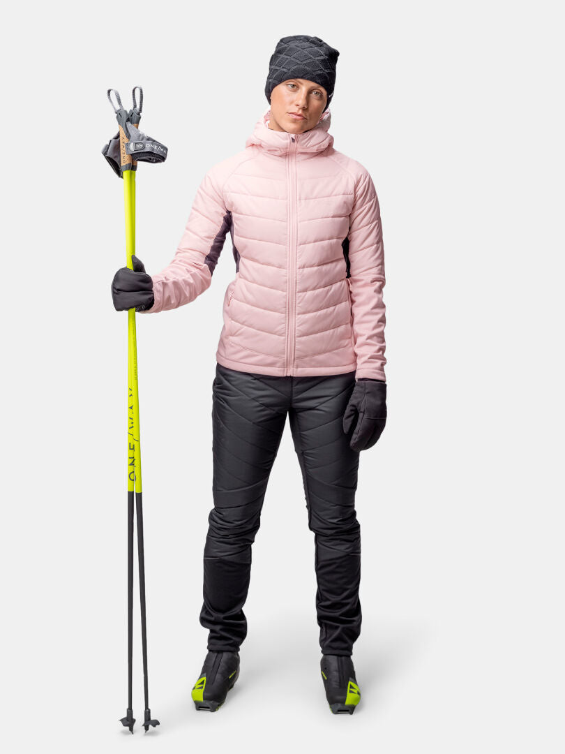 Naisella on yllään Haltin Hanki 2 Hybrid Hiihtotakki, mustat housut, hanskat, pipo, hiihtokengät ja keltaiset hiihtosauvat.