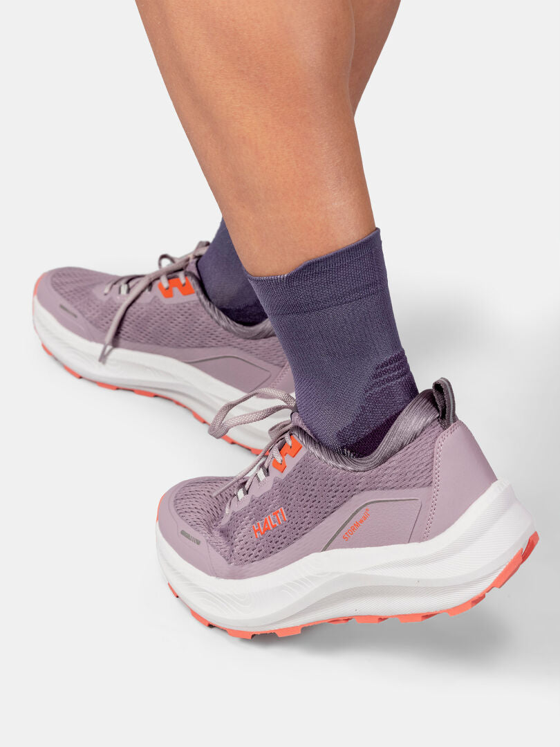Henkilö, jolla on violetit juoksukengät ja Halti Active Sport Sukat, seisoo vaaleanharmaalla taustalla.