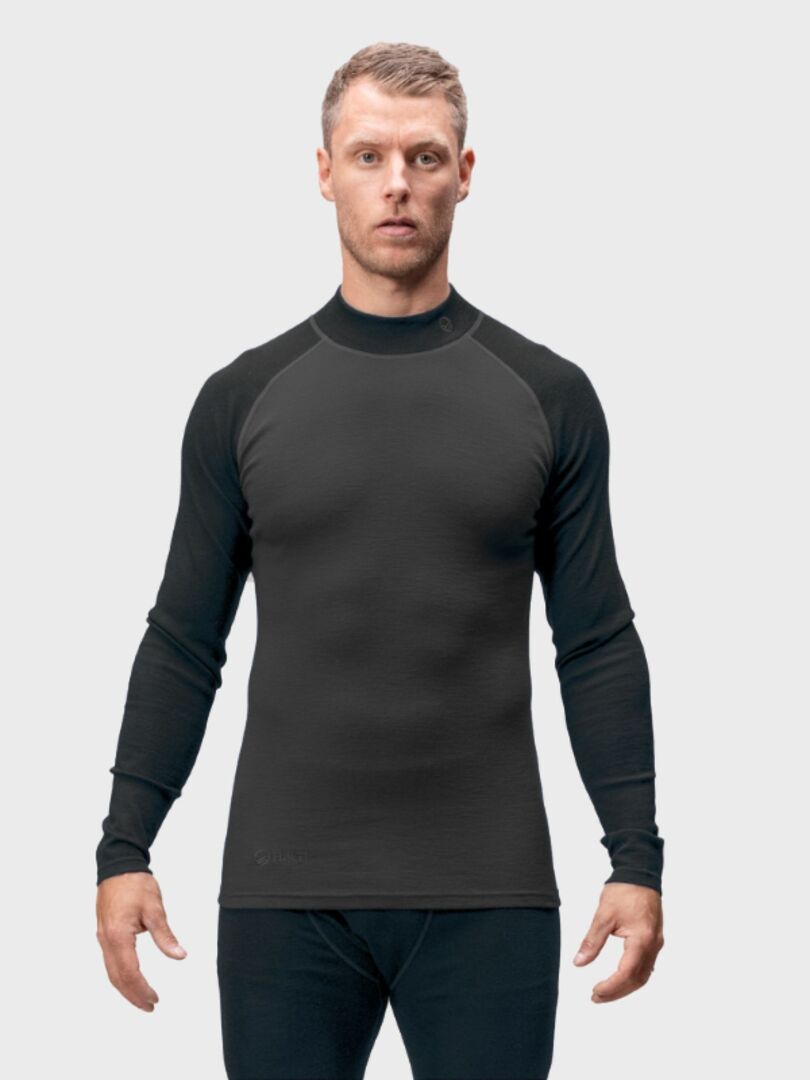 Mies, jolla on sovitettu Halti Neva Merino Kerrasto Miesten asu, seisoo tavallista vaaleaa taustaa vasten.