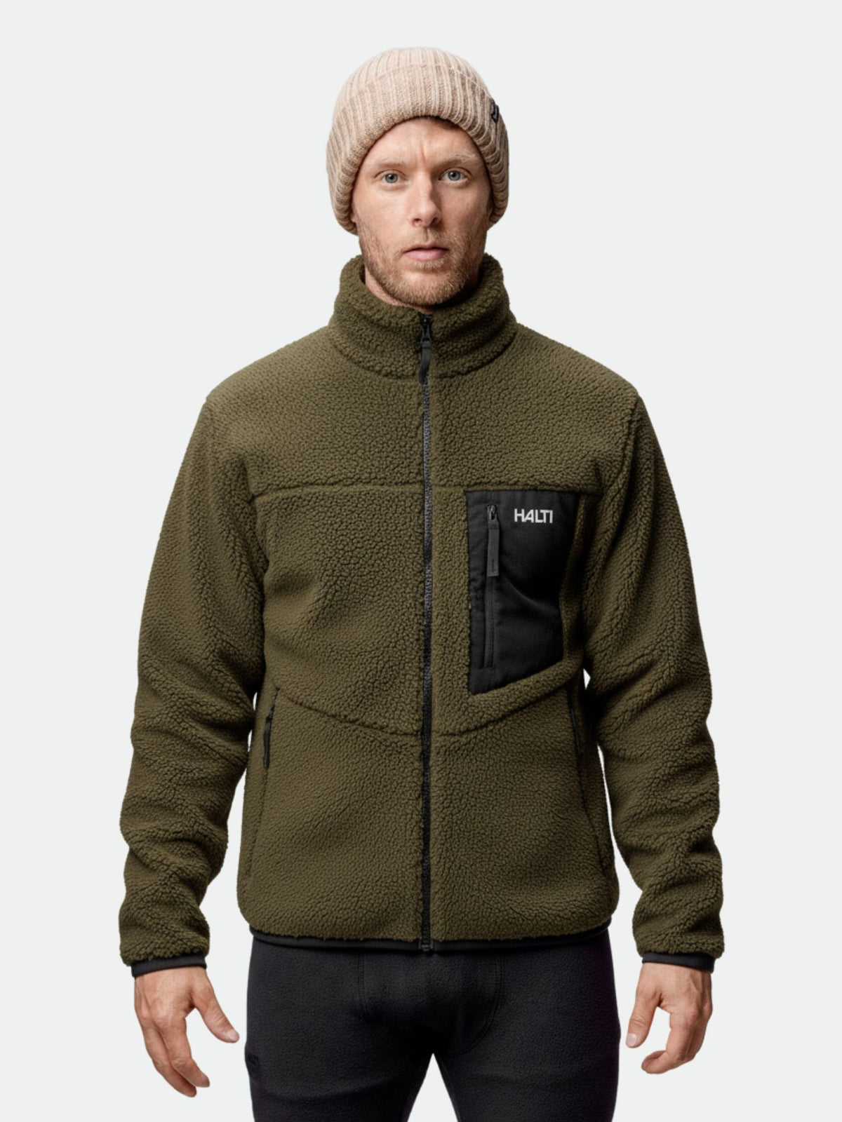 Mies, jolla on vihreä Halti Lumista Polar Fleecetakki Miesten ja beige neuletakki, seisoo kasvot menosuuntaan.