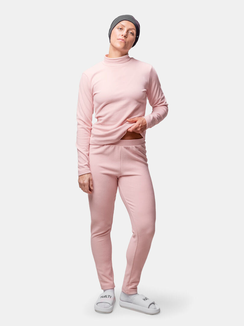 Henkilöllä on yllään Halti Trone Fleecepaita Naisten, leggingsit, harmaa pipo ja valkoiset tossut tavallista taustaa vasten.