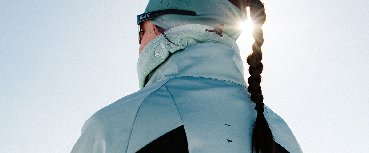 Henkilö, jolla on vaaleansininen takki ja pipo, pitkät letit, seisoo ulkona kirkkaassa auringonvalossa.
